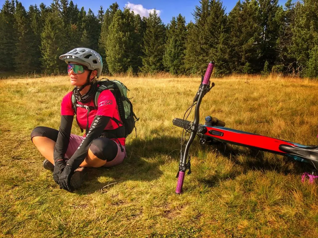 Una ciclista seduta su un prato accanto alla sua e-MTB rossa, bosco sullo sfondo