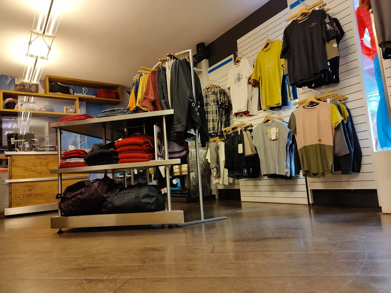Interno del negozio, reparto abbigliamento estivo con parete di magliette e tavoli
