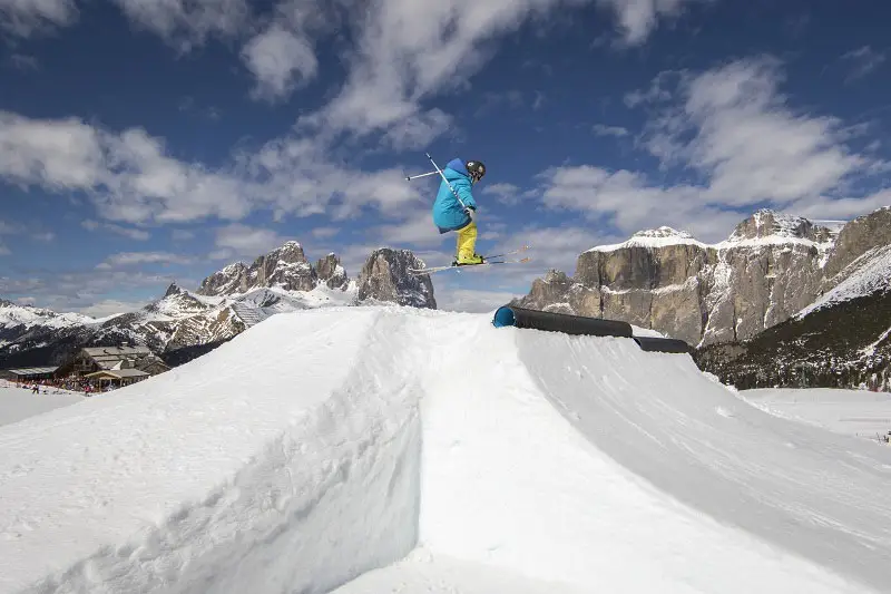 Freestyle-Skifahrer im Sprung im Snowpark Belvedere, dahinter die Sellagruppe