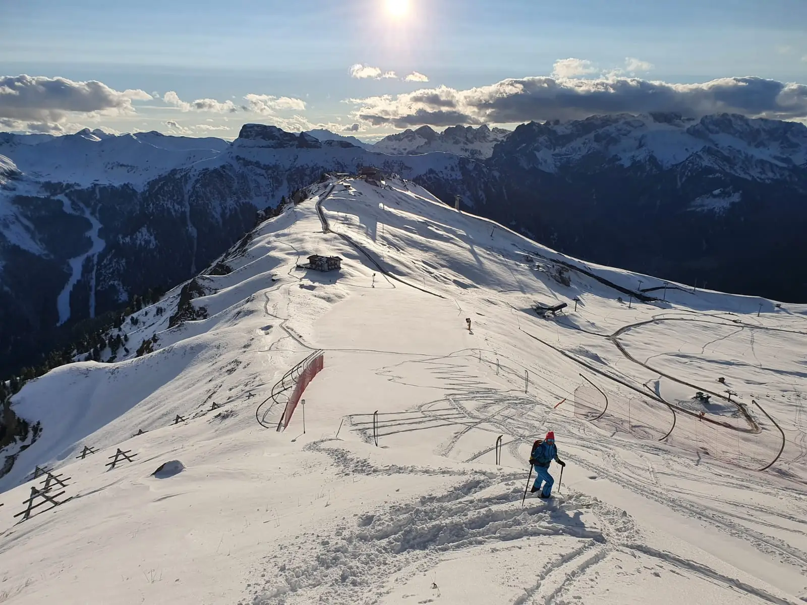 Veduta dall’alto di una cresta innevata con uno scialpinista solitario, piste battute e catene montuose