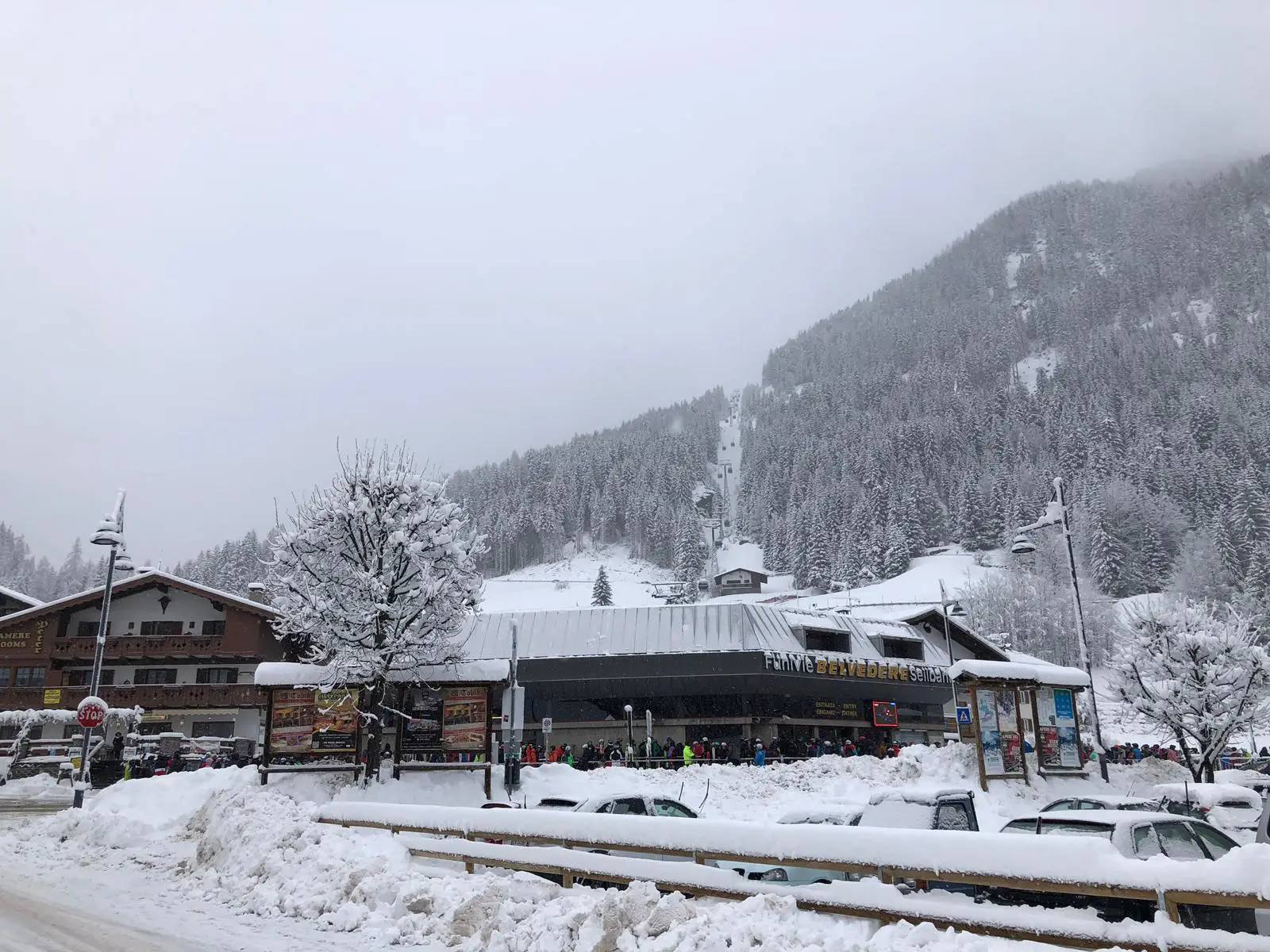 Strada innevata di Canazei con il negozio ai piedi dell’impianto di risalita, sotto la neve
