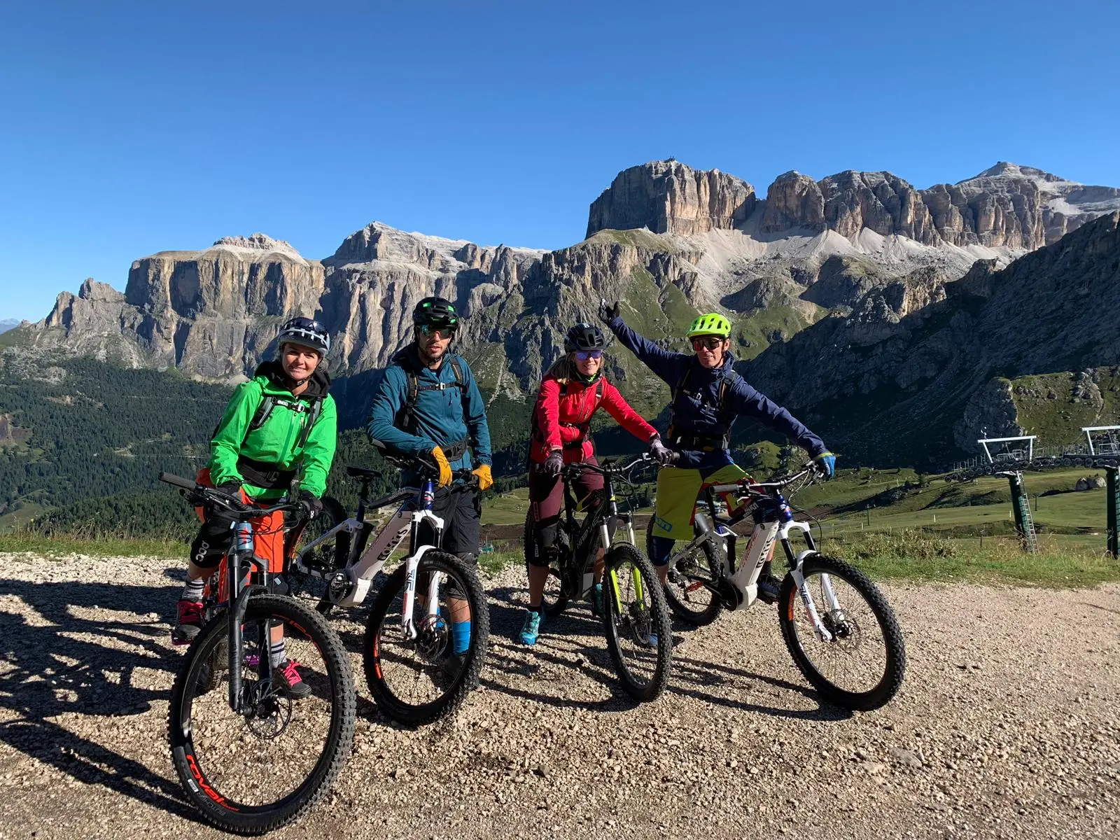 Four e-MTB riders posing with their bikes on a gravel track, Sella group behind, blue sky