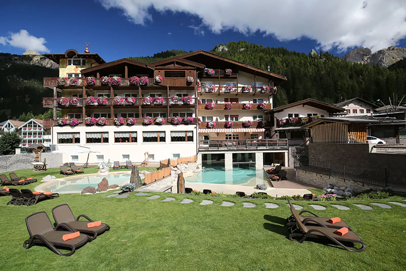 Hotel Croce Bianca, Außenansicht mit Blumenbalkonen, Außenpool und Liegen auf der Wiese