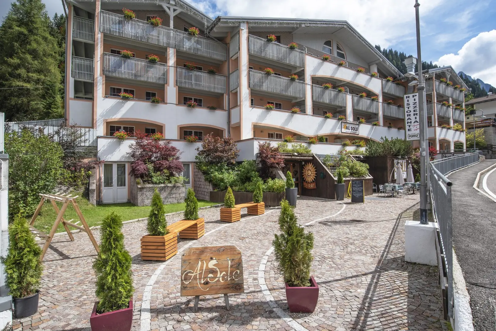 Hotel & Residence al Sole, Außenansicht im Sommer mit Kopfsteinpflaster und „Al Sole“-Schild