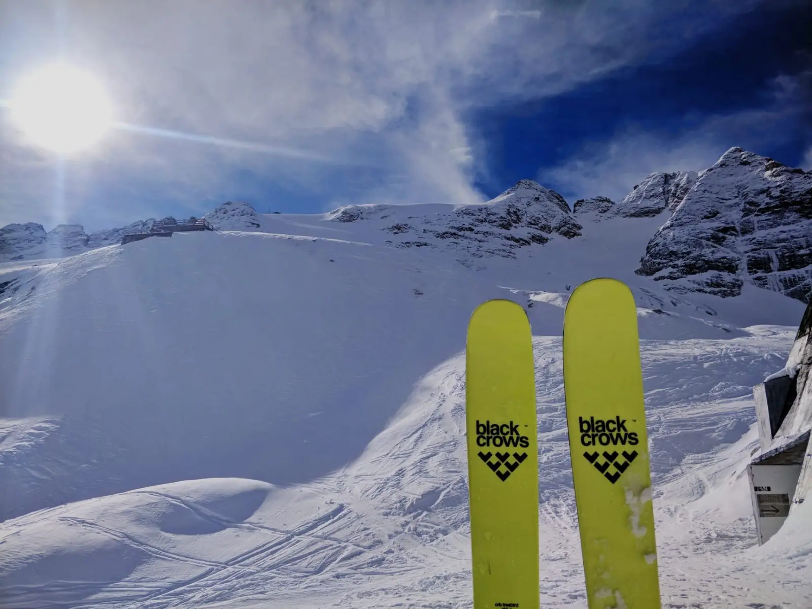 Gelbe Black-Crows-Ski aus der Sicht des Skifahrers auf einem sonnigen Schneefeld mit Gletschergipfeln