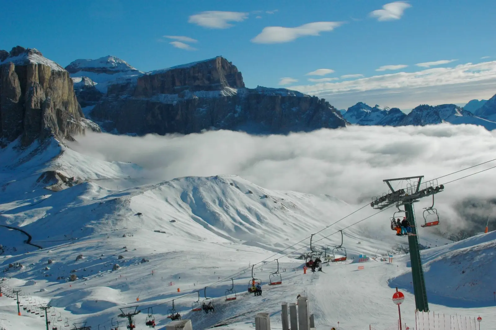 The Sella group above a sea of clouds, with a chairlift over snowy slopes