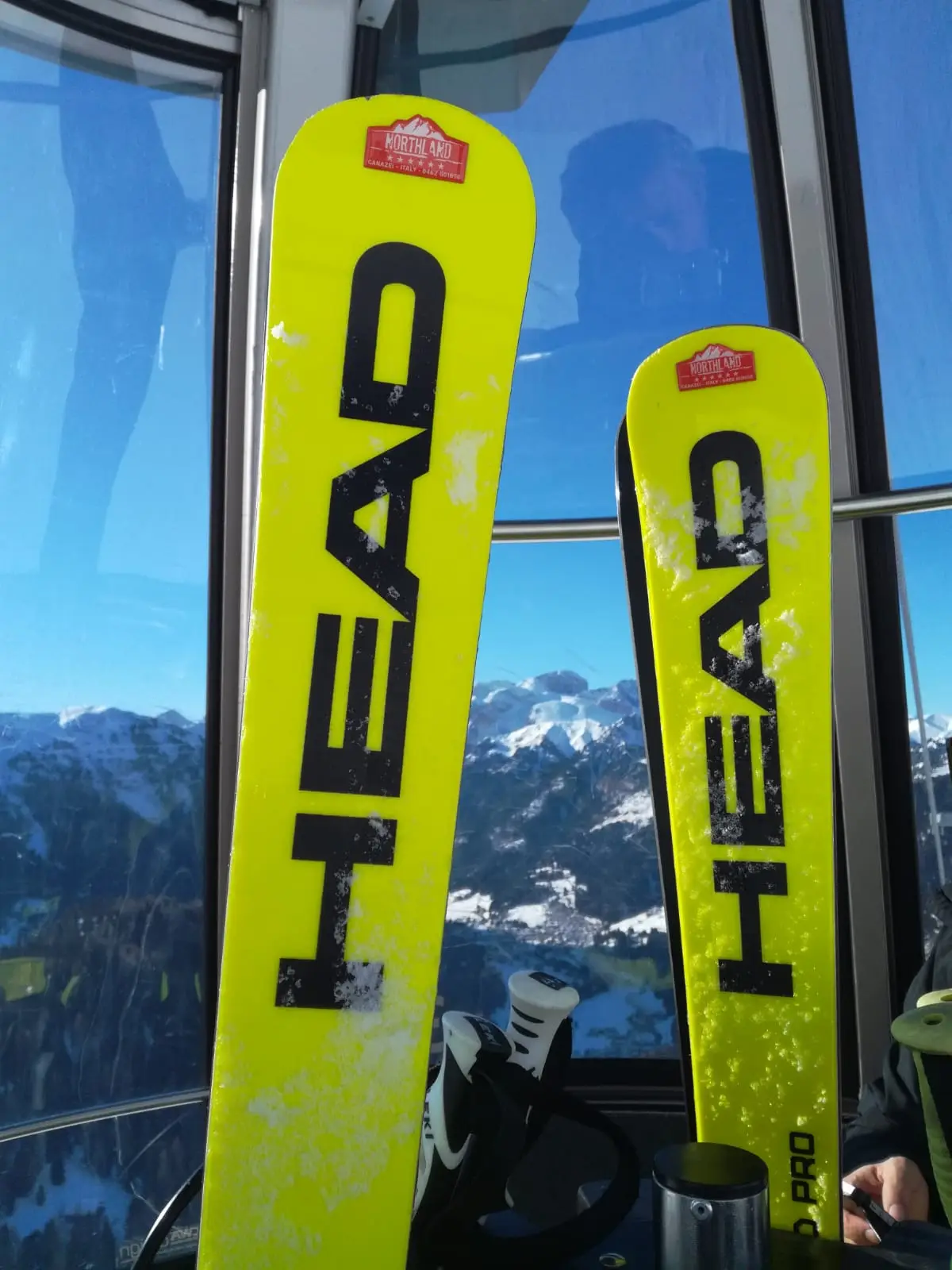 Zwei gelbe HEAD-Rennski im Fenster einer Seilbahnkabine, draußen Berge