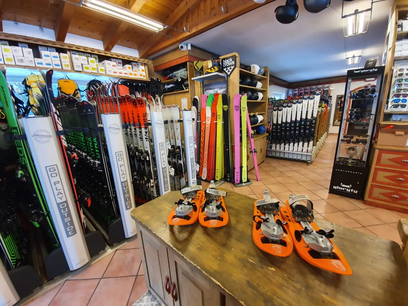 Shop interior: ski racks full of skis and orange snowshoes on the wooden counter