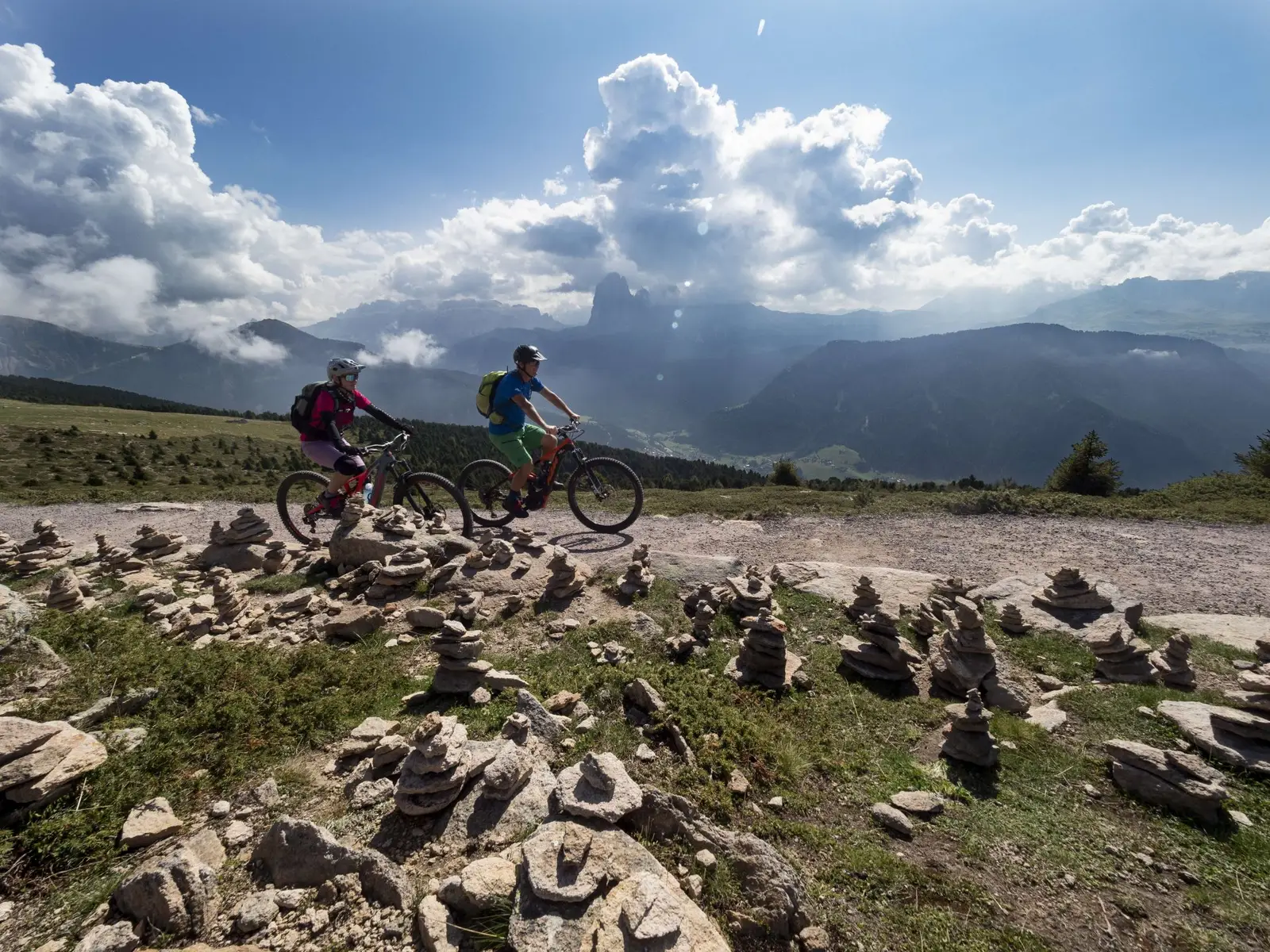 Zwei E-MTB-Fahrer auf einem felsigen Plateau mit Steinmännchen und Wolken