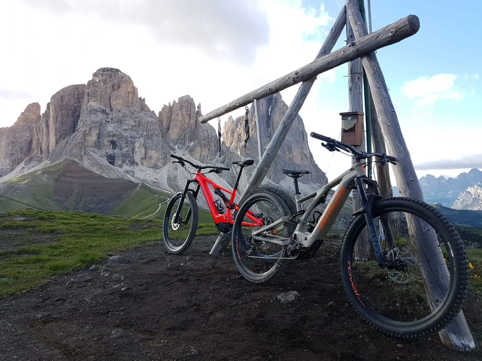 Two e-MTBs leaning on a wooden summit cross, Sassolungo in the background