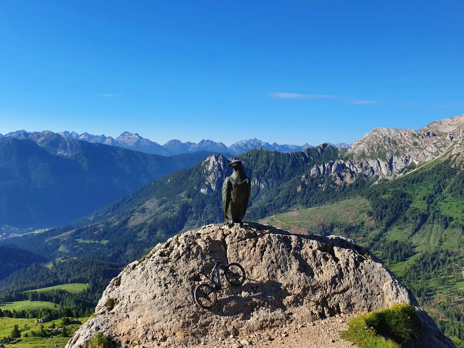 Statua di un’aquila su uno sperone di roccia con una bici scolpita, panorama sulla valle