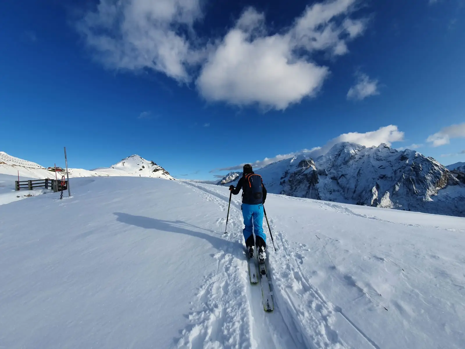 Scialpinista in salita con le pelli su un pendio innevato sotto un cielo blu intenso, cime davanti