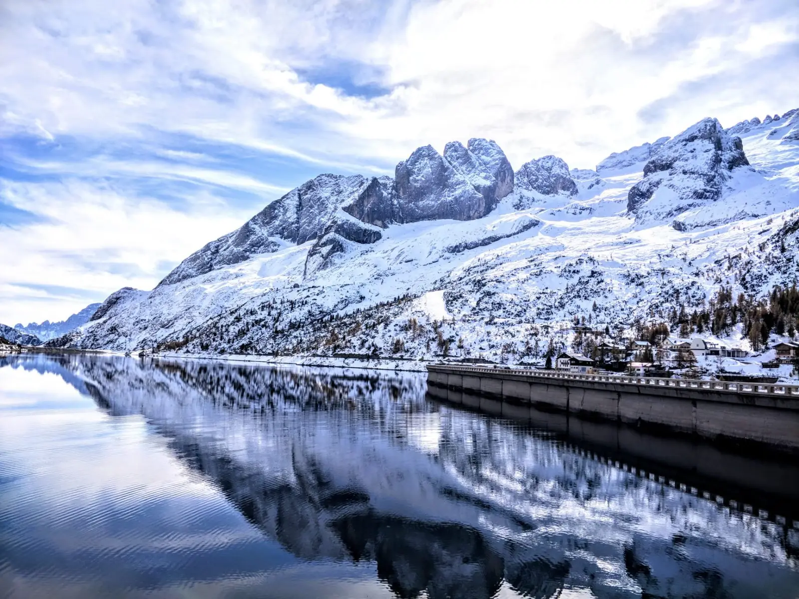 Der Fedaiasee mit der verschneiten Marmolada, die sich im Wasser spiegelt, rechts die Staumauer